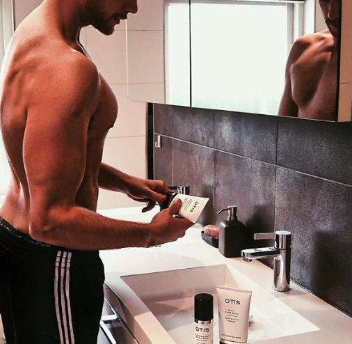 Handsome young man standing at sink opening a Tube of OTIS Protective Shave Cream