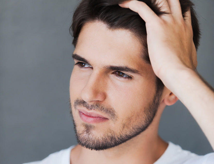 Handsome young man with clear skin looking away while standing against grey background