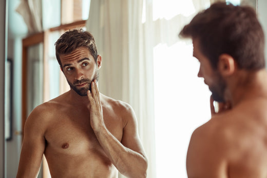 5 Signs You Need to Switch Up Your Skincare Routine. Handsome man worried about his skin looking in the mirror