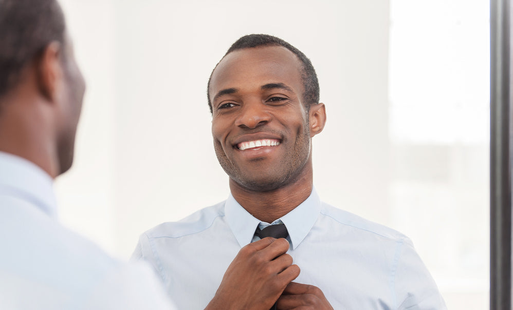 Handsome black man looking in mirror adjusting his tie