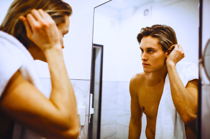 Breakouts and Dryness? Here’s How to Balance Your Skin. Young man looking at his skin in mirror