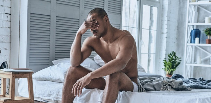 How Stress, Sleep, and Your Gut Are Showing Up on Your Skin. Handsome black man sitting on bed after a bad night's sleep