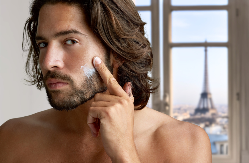 How French Skincare Can Take Your Routine to the Next Level. Parisian man applying moisturizer with view of Paris behind