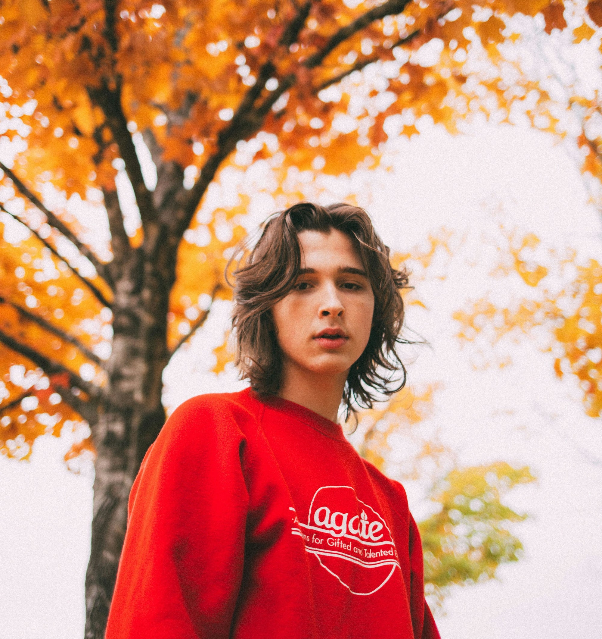 How to Buy Skincare for Your Son: A Parent’s Guide to Getting Teenage Skin Right. Teenage boy in red sweatshirt looking unsure of himself