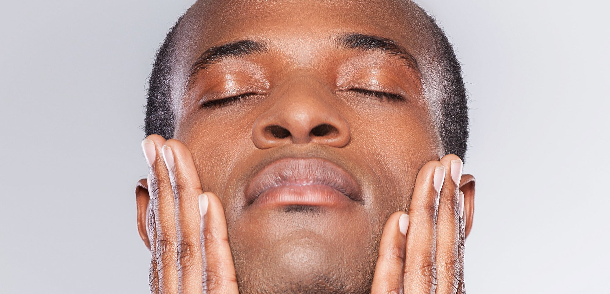 A Dermatologist’s Guide to Evening Out Dark Spots and Hyperpigmentation. Close up of handsome black man stroking his face