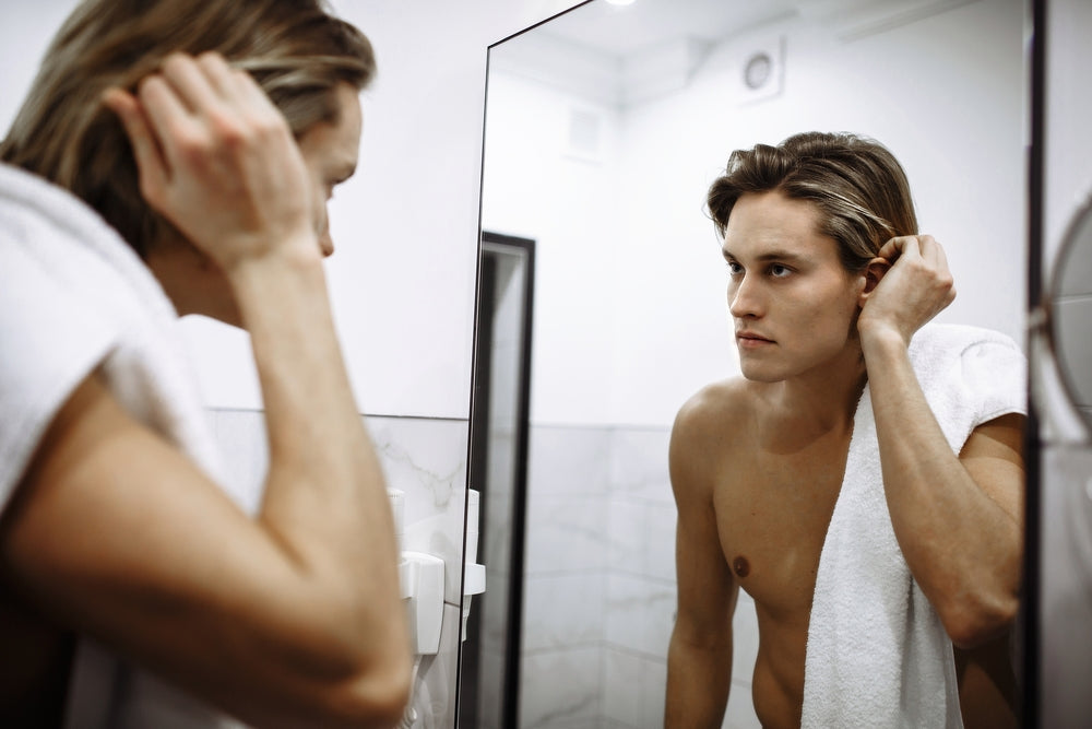 ADUNLT ACNE. Man looking in mirror checking his face for breakouts