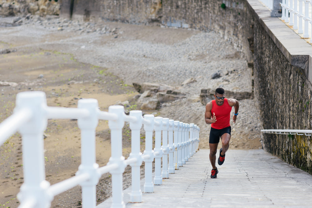 healthy fit young man running up slope wearing red vest