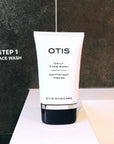 White tube of OTIS Daily Face Wash against charcoal gray tiles